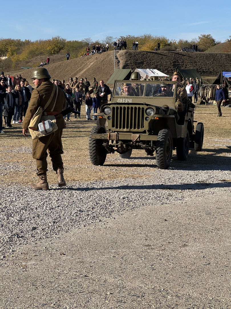 A reenactor running alongside a moving WWII jeep loaded with soldiers in uniform