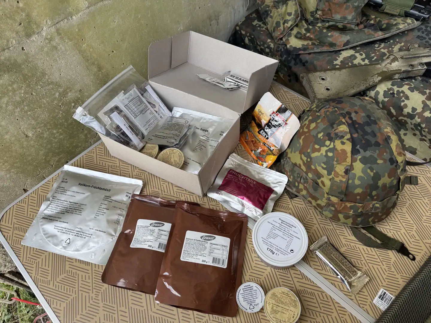 Field rations laid out beside a camouflage helmet and pack