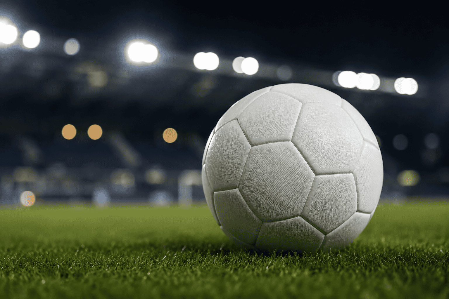A football on the pitch under stadium lights