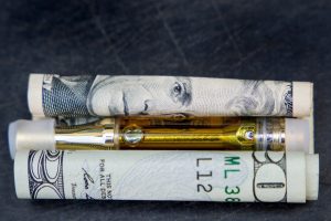 $100 bill, vape pen, and rolled-up dollar bills on dark surface - vaping, vape deals, and financial savings.