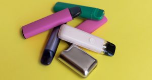 Assorted disposable vape pens and devices on a yellow background.