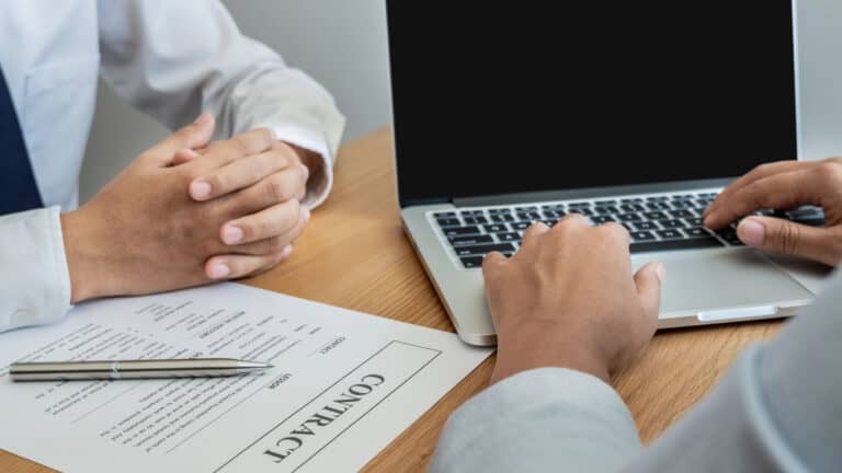 Business meeting with legal documents and laptop on a wooden table.