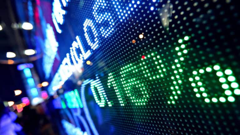 Stock market ticker display with green and blue lights in a financial district.