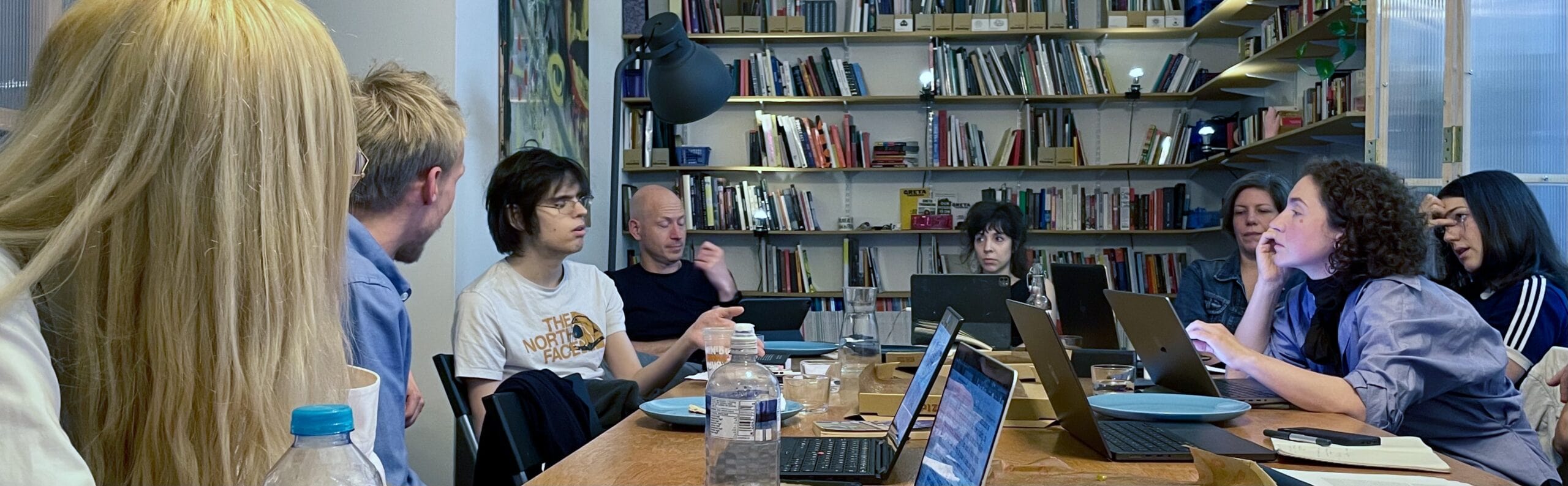 People having a meeting in a library or office with laptops, bookshelves in the background, diverse group, collaborative workspace, team discussion, modern interior design.