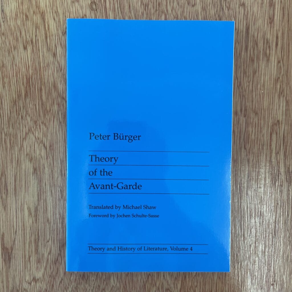 A blue hardcover book titled "Theory of the Avant-Garde" by Peter Bürger, translated by Michael Shaw, with a foreword by Jochen Schulte-Sasse, on a wooden surface.