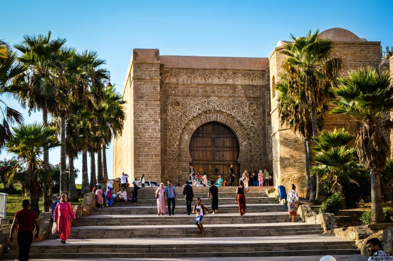 Detailed view of the ancient Moroccan fortress gate with visitors and lush palms.