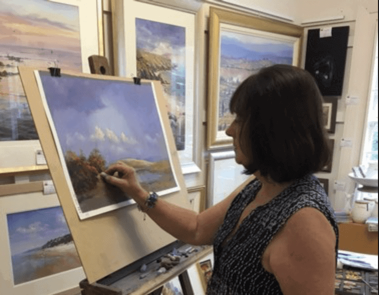 Artist creating a pastel landscape painting in an art studio.