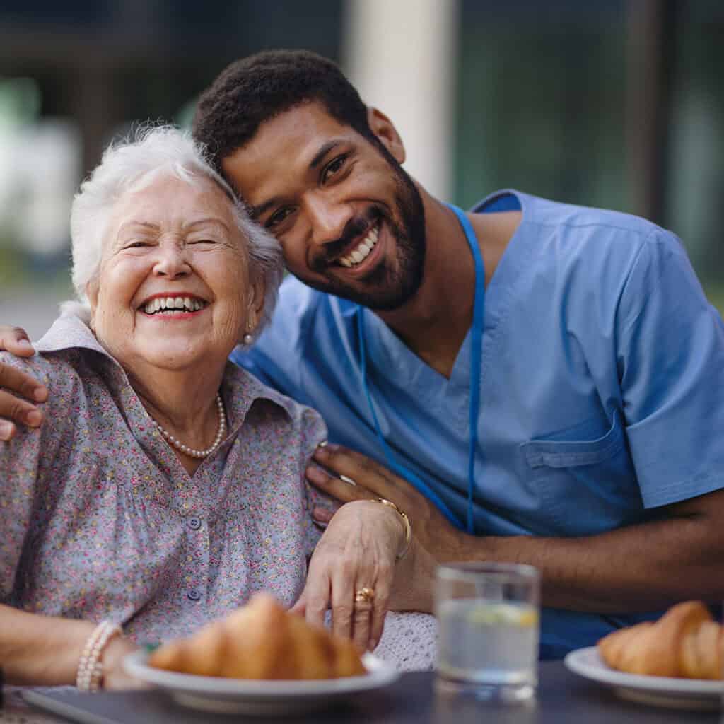 Elderly woman smiling with caregiver at Vineyard Park Senior Living facility.