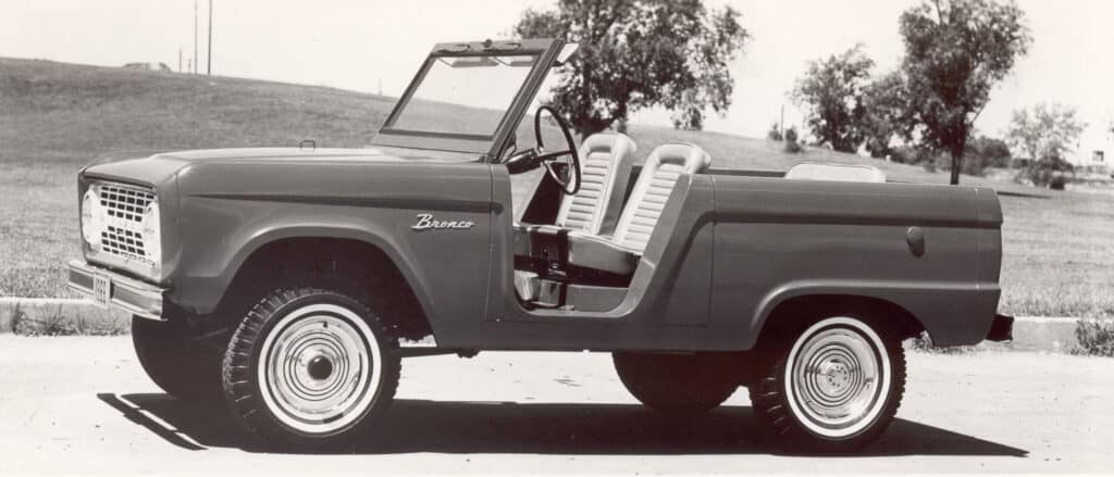 Vintage vintage Ford Bronco classic car with open side view, black and white photograph, retro style, outdoor setting in the countryside, historical automobile design.