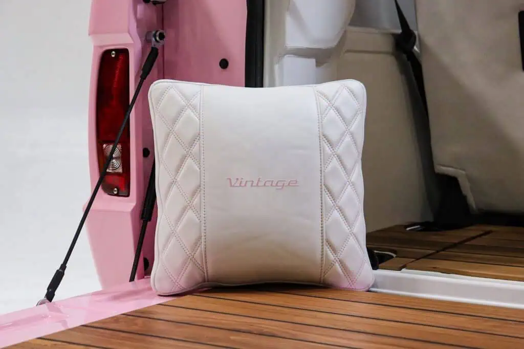 Vintage modern white quilted pillow with "Vintage" embroidery on a wooden deck with a pink boat interior in the background.
