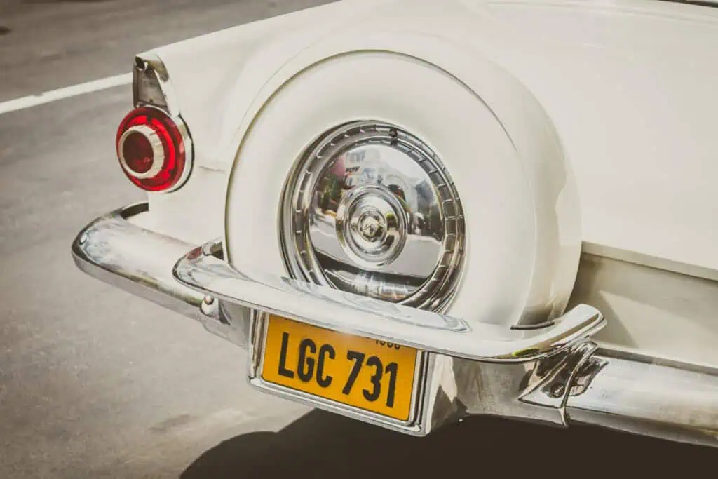 Vintage car tail light and chrome bumper with yellow license plate in classic style.