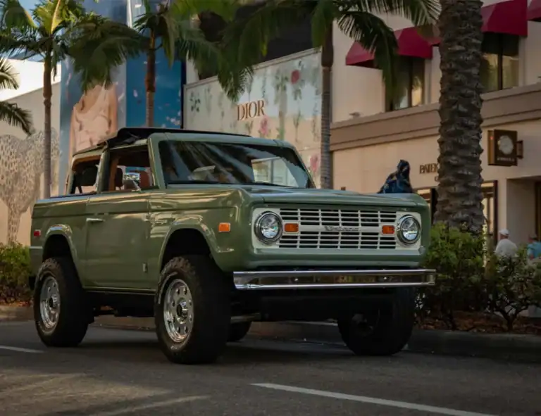 Vintage green off-road vehicle parked near palm trees and luxury boutiques.