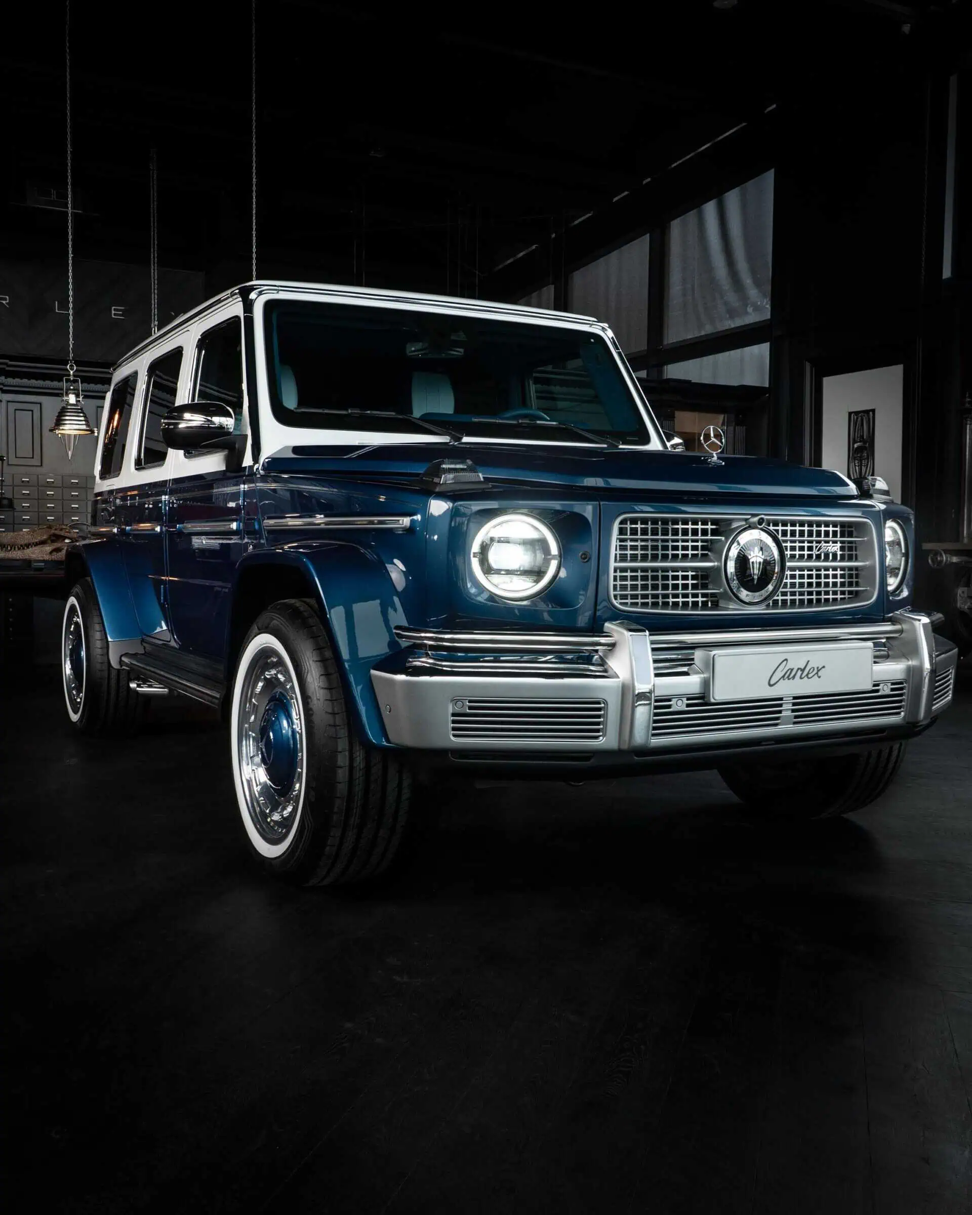 A classic blue and white vintage SUV displayed in a modern showroom with sleek lighting and dark flooring, highlighting retro style and luxury design.
