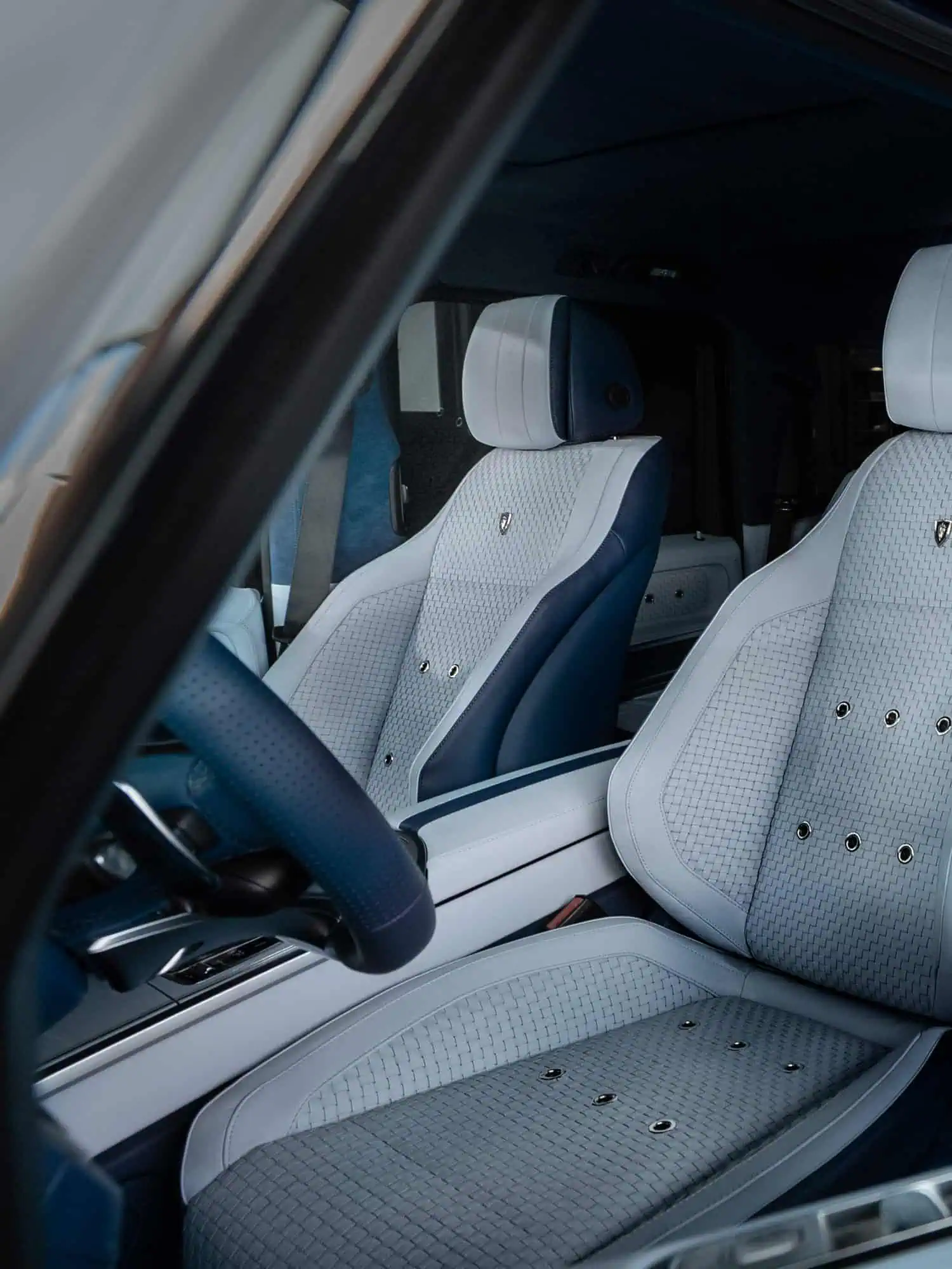 Modern luxury vehicle interior featuring custom white and navy leather seats with intricate detailing and high-end finishes.