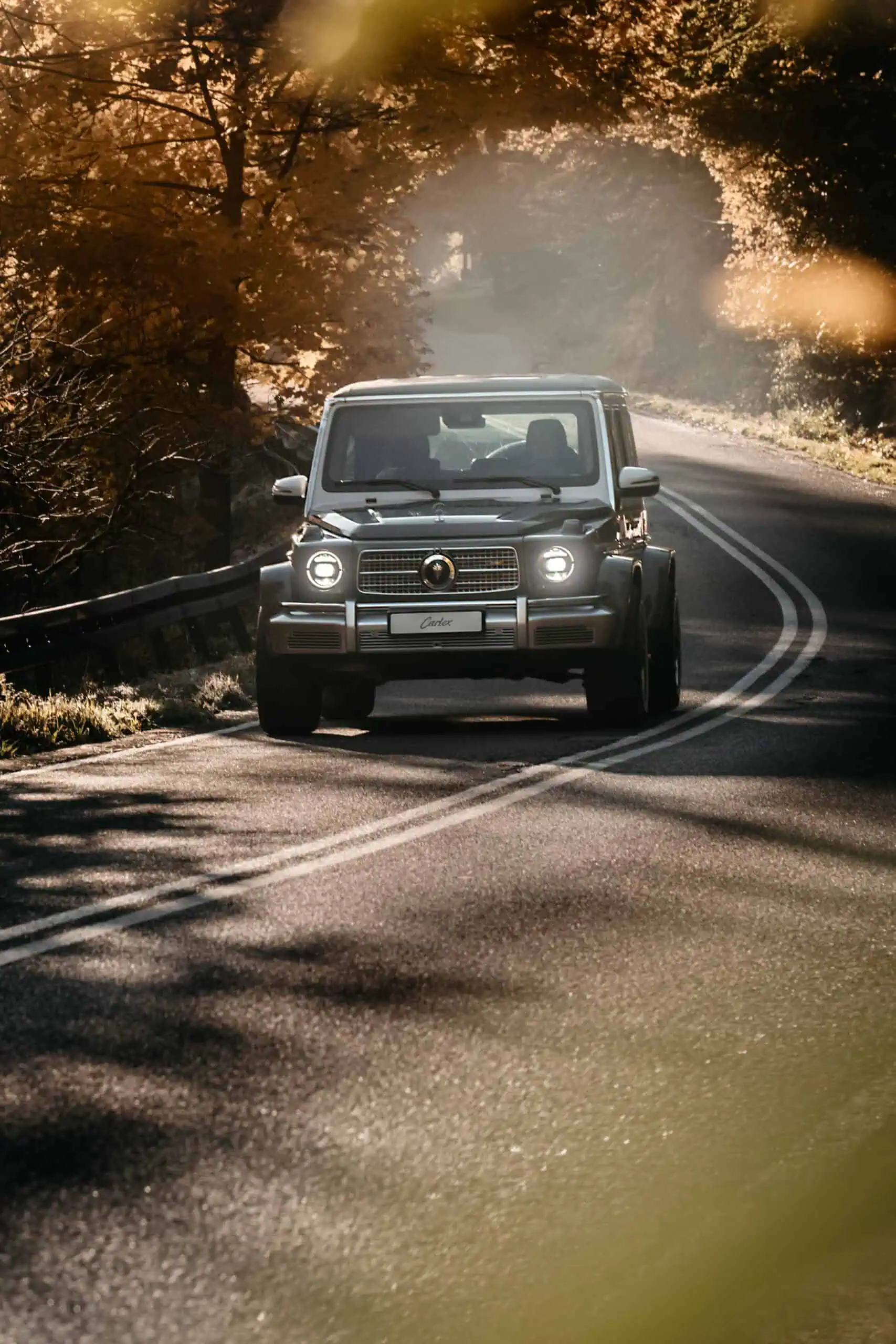 A classic vintage mini car driving along a scenic, winding mountain road surrounded by autumn trees with golden foliage, capturing timeless style and adventure.