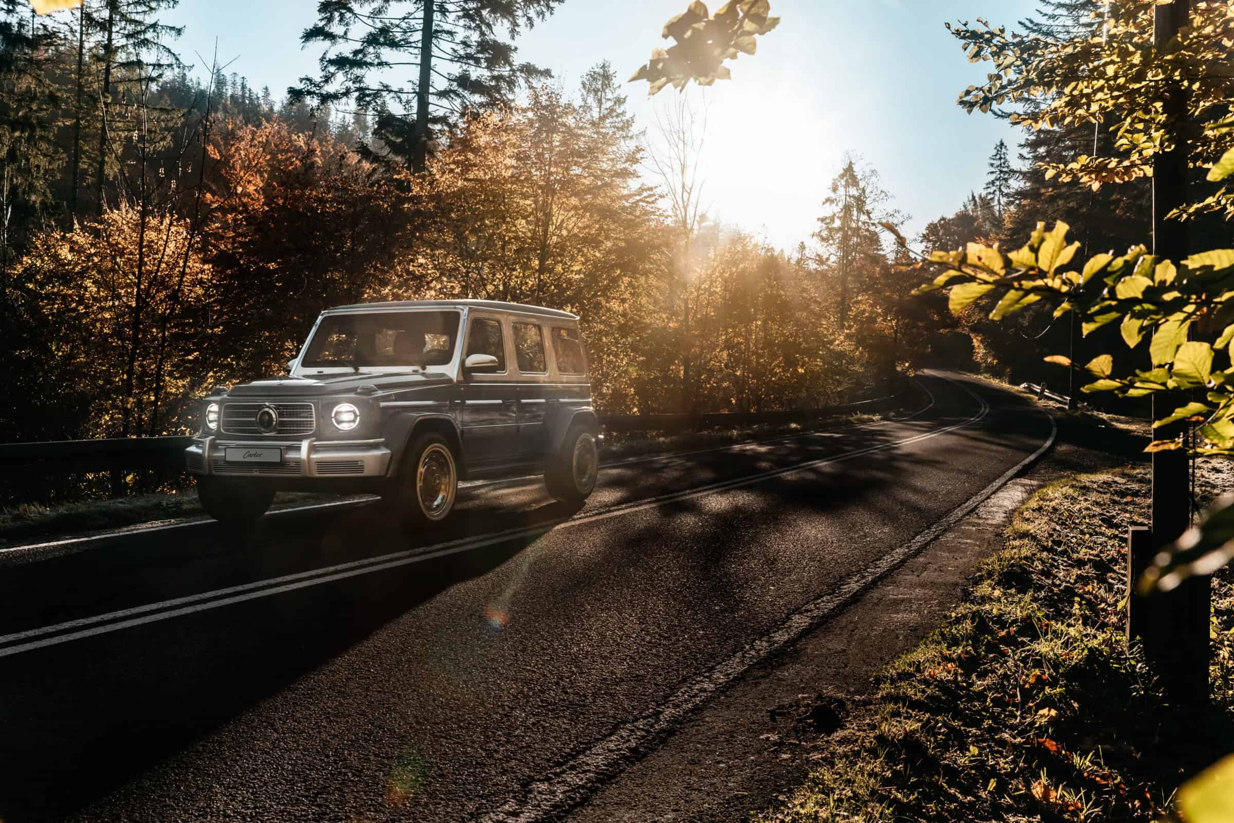 A vintage SUV driving along a winding mountain road surrounded by vibrant autumn foliage and basking in warm sunlight, creating a timeless and adventurous atmosphere.