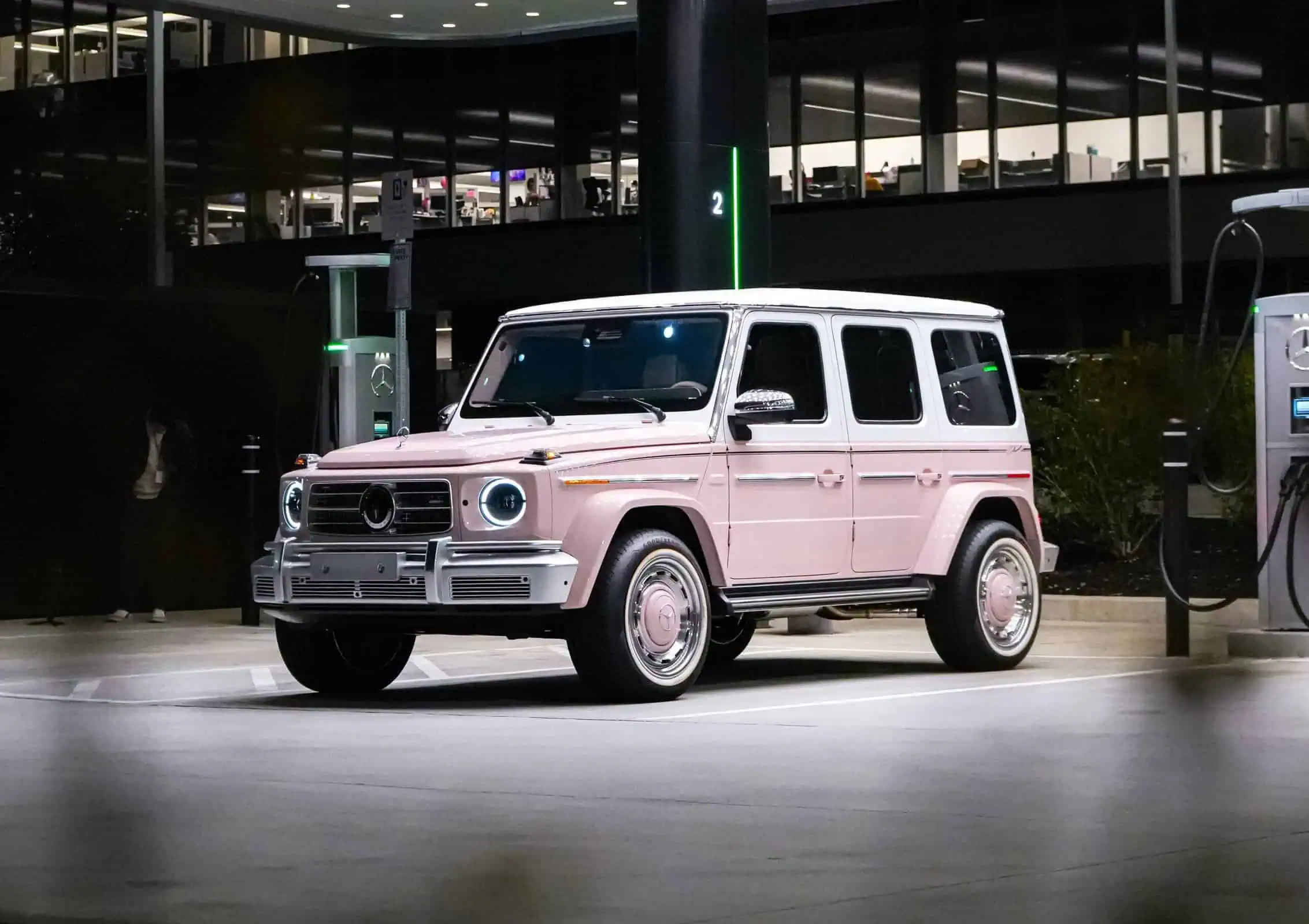 A classic Mercedes-Benz G-Class in pink parked at an electric vehicle charging station, showcasing a blend of vintage style and modern electric car innovation.