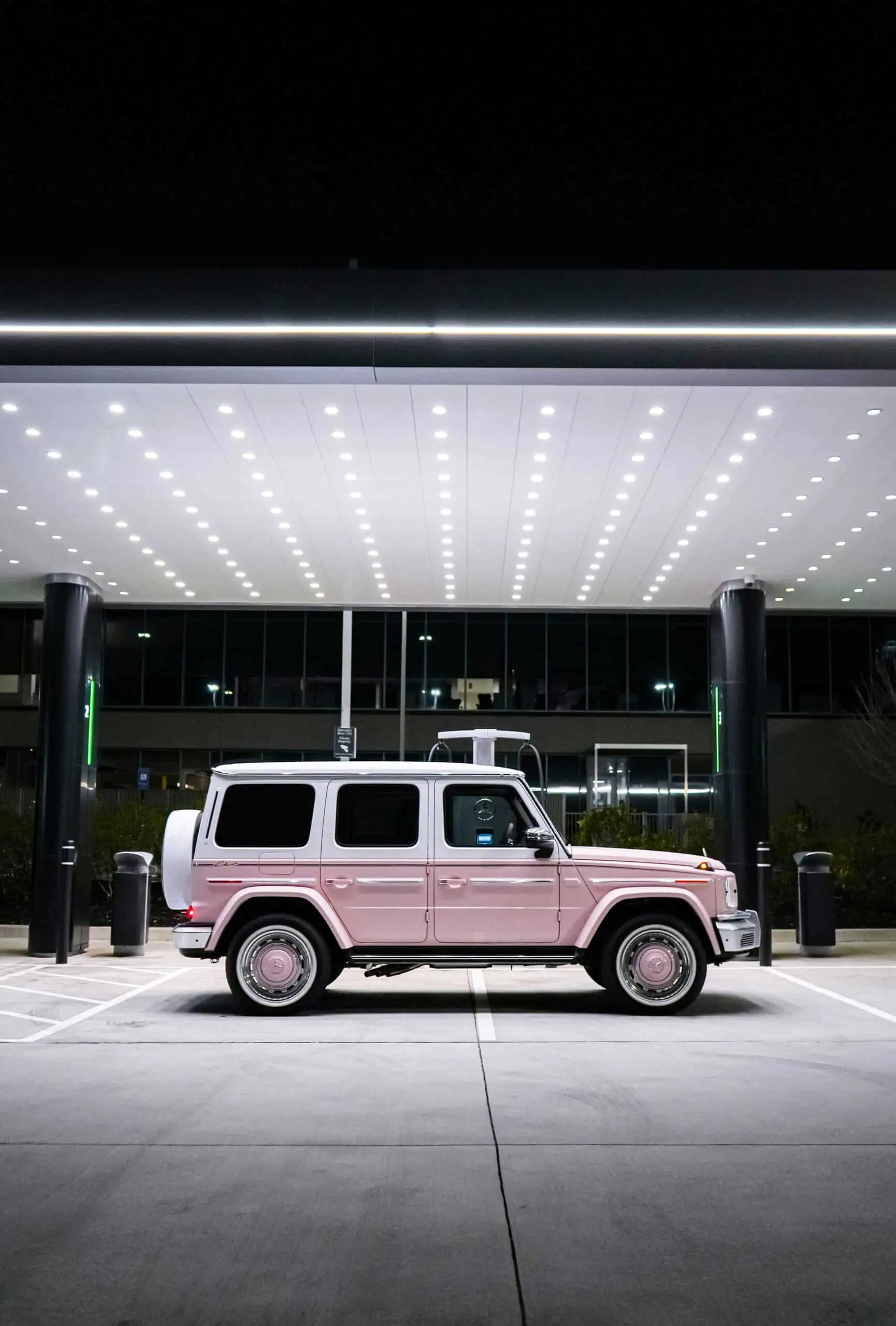 A white vintage SUV parked at night beneath a sleek, modern canopy with bright LED lighting, showcasing contemporary architectural design and classic vehicle style.