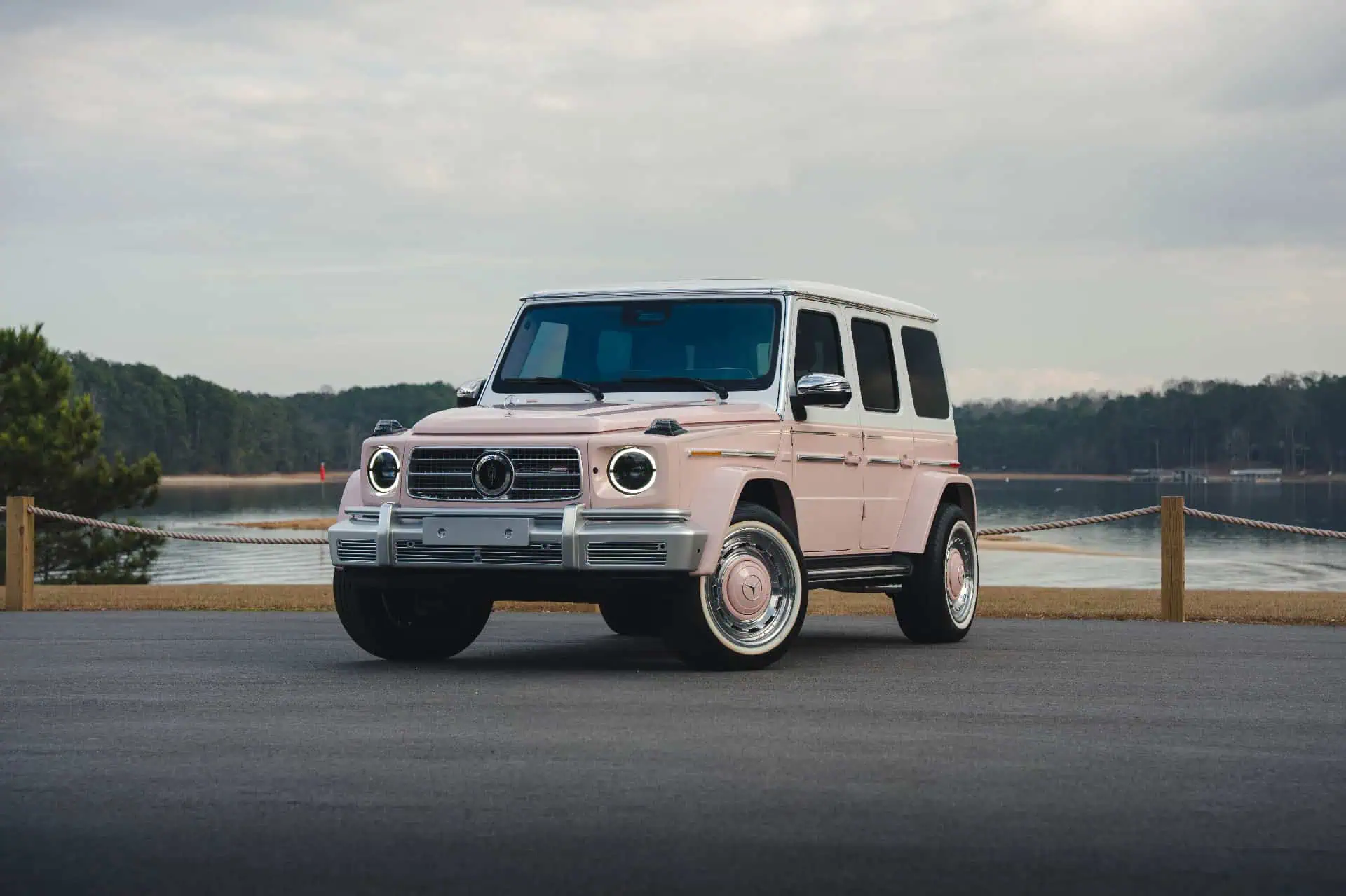 A vintage pink and black Mercedes-Benz G-Class SUV parked by a lake, showcasing modern retro style with classic design elements. Perfect for vintage modern decor.