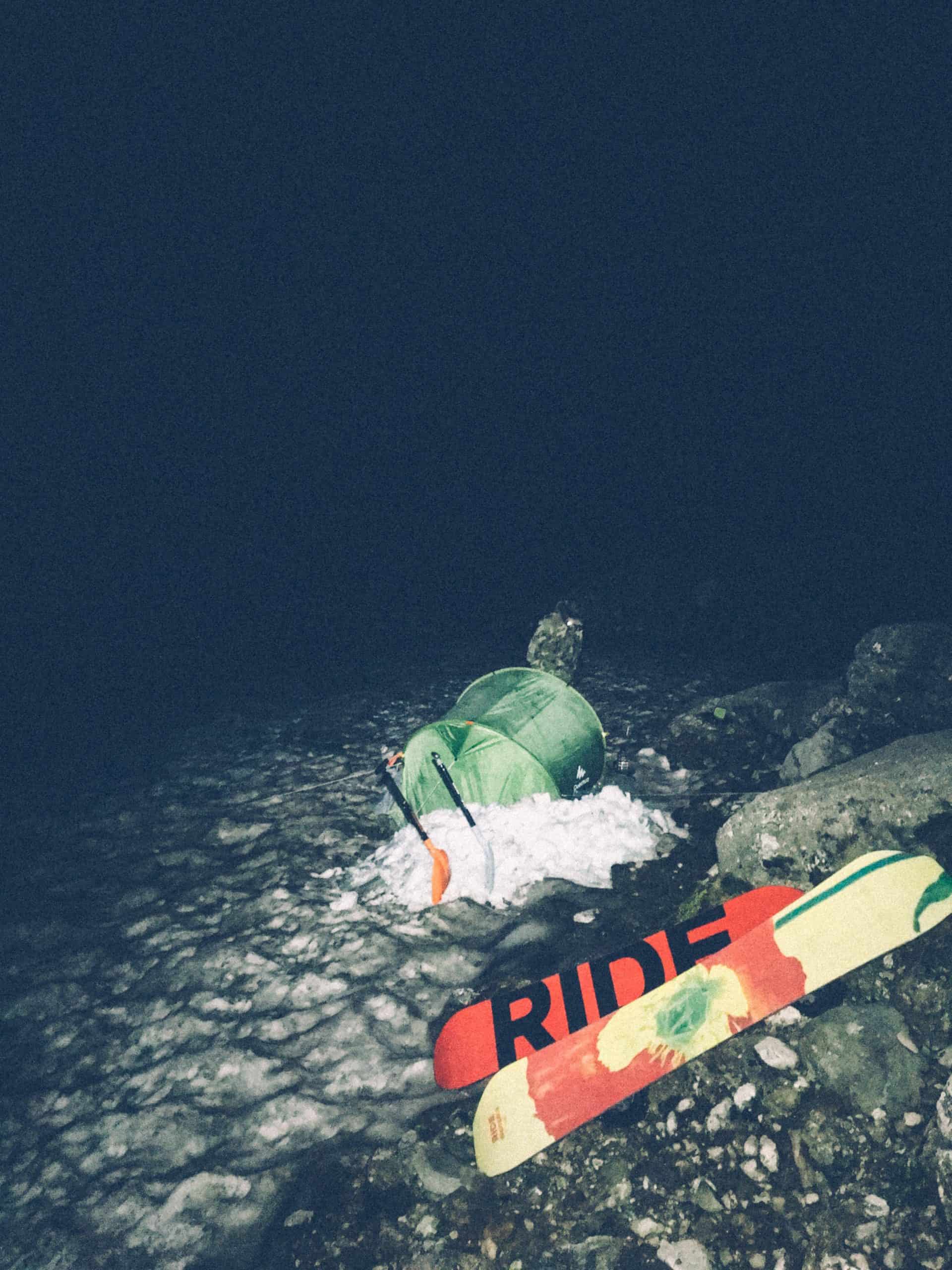 Nighttime winter water rescue scene with a person in a green dry suit near rocks.