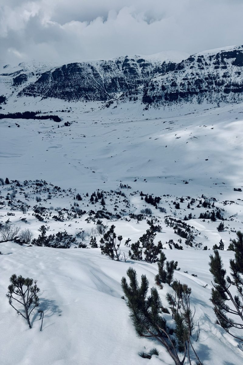 Snowy mountain valley with rugged cliffs and cloudy sky.