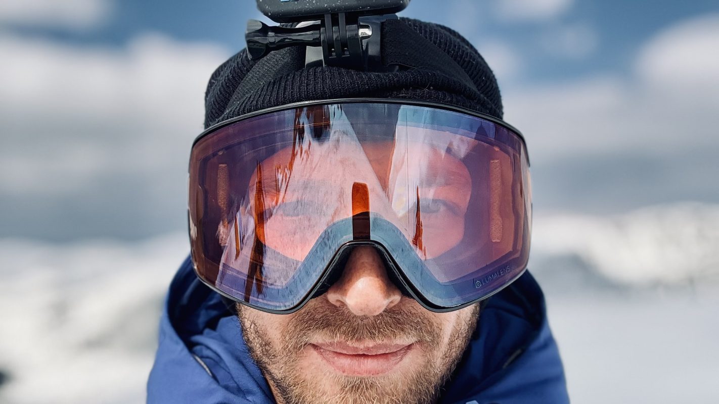 Viorel Corbu - Aventură în zăpadă Viorel Corbu purtând ochelari de snowboard, în peisaj montan cu zăpadă și cer senin.