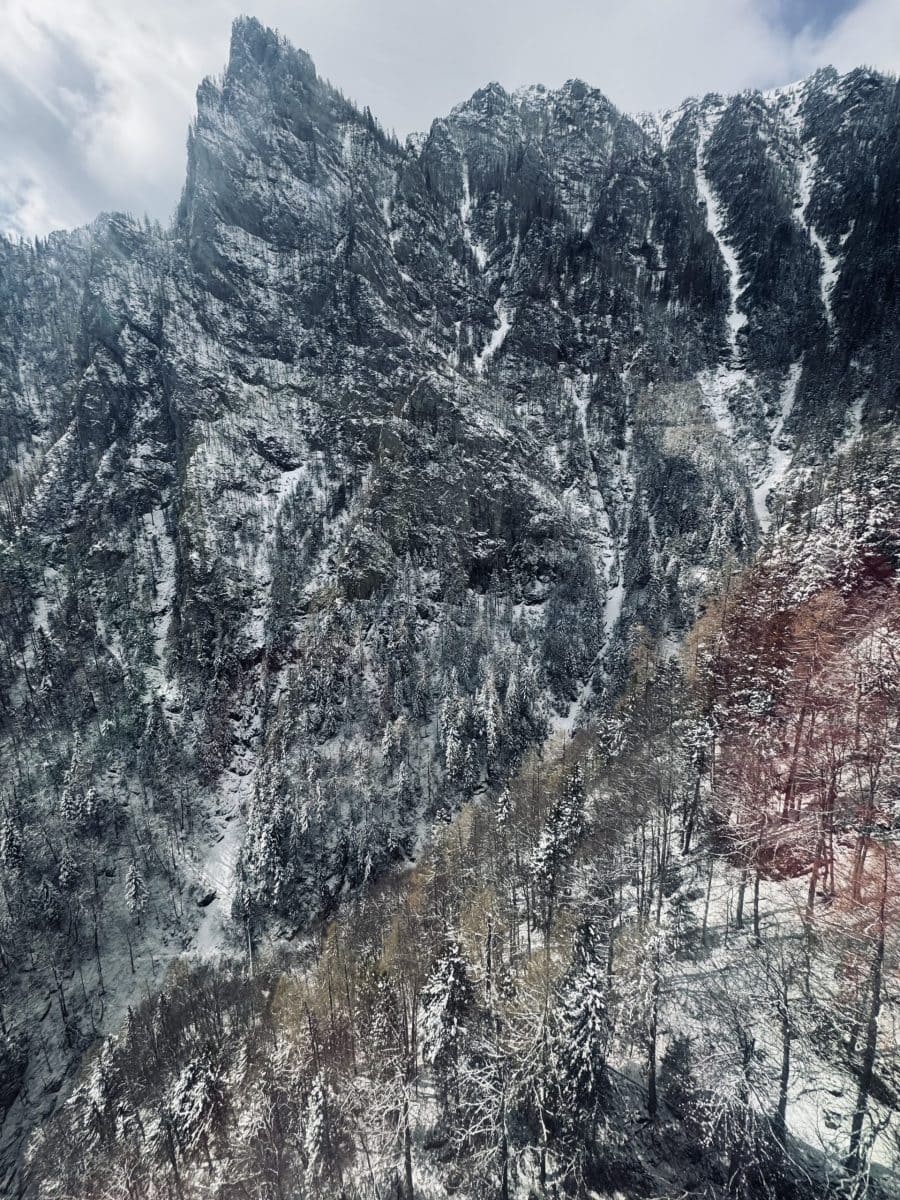 Vârfuri montane impresionante acoperite de zăpadă, în peisaj de iarnă, cu stânci abrupte și pădure d.