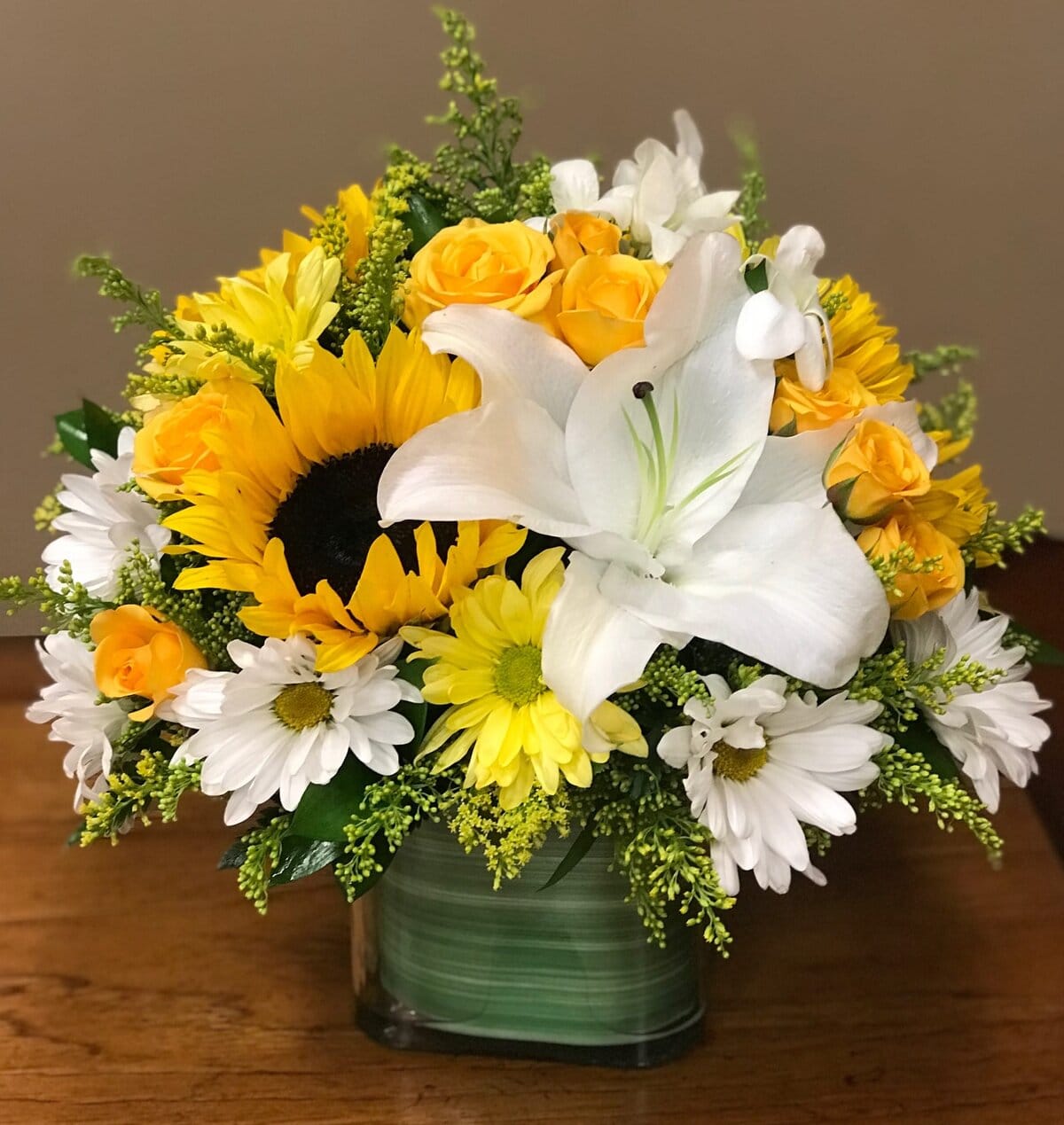 As joyful as the laughter of a good friend, this mood-lifting mix of yellow roses and white lilies is artistically arranged in our exclusive Color Splash cube for a look that's modern and playful. What a stylish way to make someone's day! This cheerful bouquet features yellow roses, sunflowers, white lilies, white daisies, yellow daisies, yellow solidago, green ruscus.