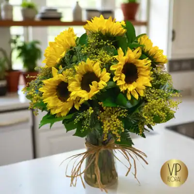 Sunflower bouquet in a glass vase with green foliage, perfect for brightening any space or special occasion.