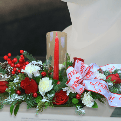 Introducing our "Christmas Cheer Centerpiece" – a festive blend of red roses, white carnations, and pinecones, complemented by a merry Christmas bow and a glowing red candle. Elevate your holiday table with this enchanting arrangement, radiating the spirit of the season.