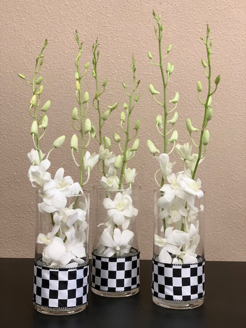 Elegant white Dendrobium orchids arranged in tall glass vases with black and white checkered bases, perfect for sophisticated events.
