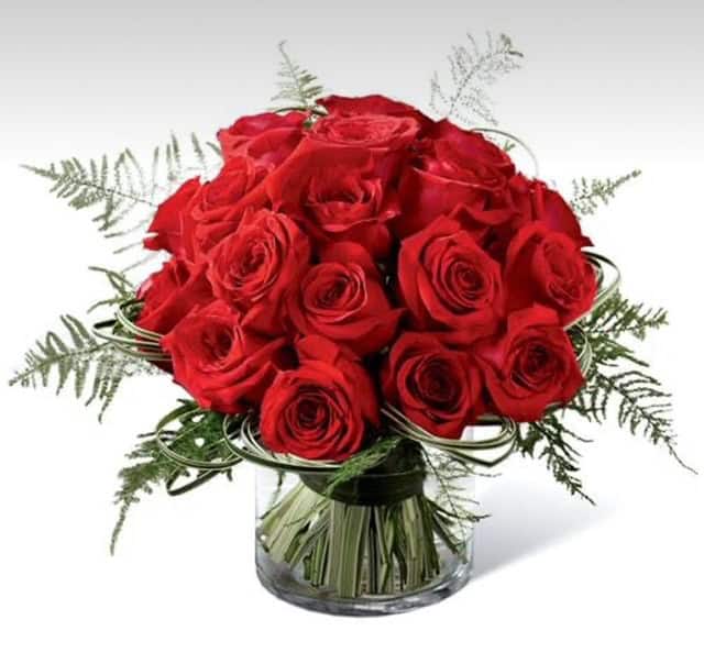 Elegant bouquet of red roses with greenery in a clear glass vase, perfect for special occasions or romantic gestures.