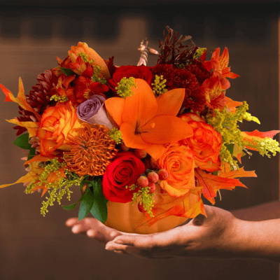 Vibrant autumn-themed floral arrangement in a copper pot with orange, red, purple, and yellow flowers and foliage, perfect for fall celebrations or gifting.