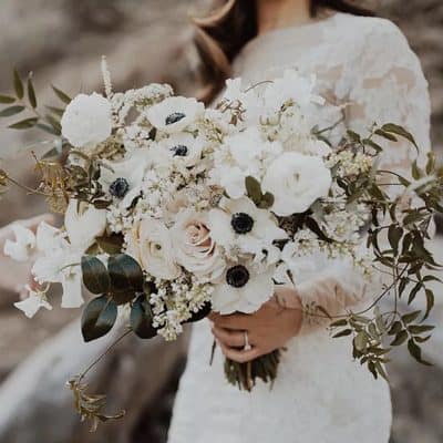 White floral wedding bouquet with roses, anemones, and greenery held by a bride in a lace dress. Perfect for bridal arrangements or special occasions in Las Vegas.
