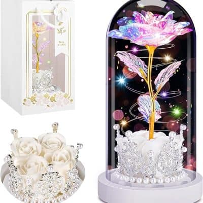 Illuminated artificial flower in glass dome with pink and purple petals, surrounded by sparkling lights and decorative silver crown base.