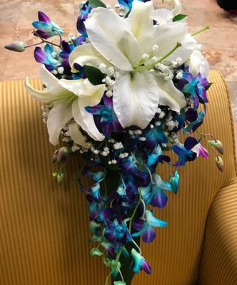 A stunning floral arrangement featuring white lilies and vibrant purple and blue orchids with a white candle, perfect for elegant events and special occasions in Las Vegas.
