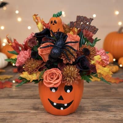 Halloween flower arrangement in jack-o-lantern pumpkin vase with orange roses, burgundy chrysanthemums, black spider, and Happy Halloween pick delivered in Las Vegas