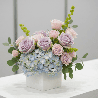 Blush & Blue Luxe Cube centerpiece with pastel blue hydrangeas, Cool Water roses, pink roses, molucella, and eucalyptus in a white cube vase