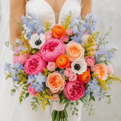 Sunrise Garden Bridal Bouquet by VIP FLORAL – Las Vegas bridal bouquet with pink garden roses, blue delphinium, peach roses, orange ranunculus, white anemones, and yellow solidago