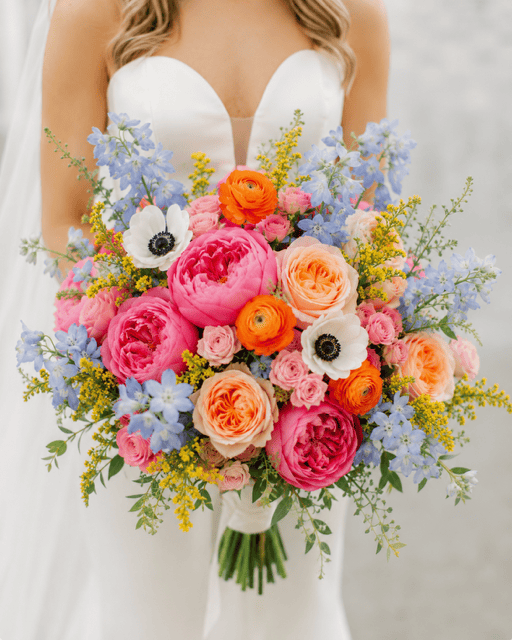 Sunrise Garden Bridal Bouquet by VIP FLORAL – Las Vegas bridal bouquet with pink garden roses, blue delphinium, peach roses, orange ranunculus, white anemones, and yellow solidago