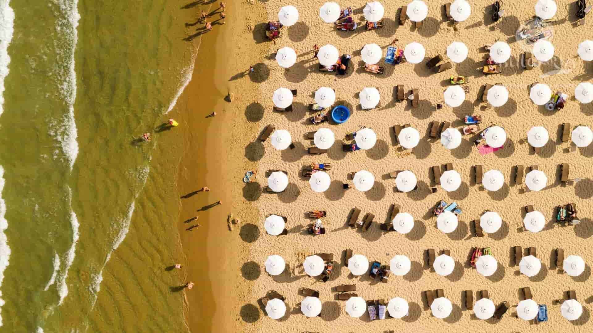 Aerial view of people enjoying a sunny day at the beach, with turquoise waters and golden sand.