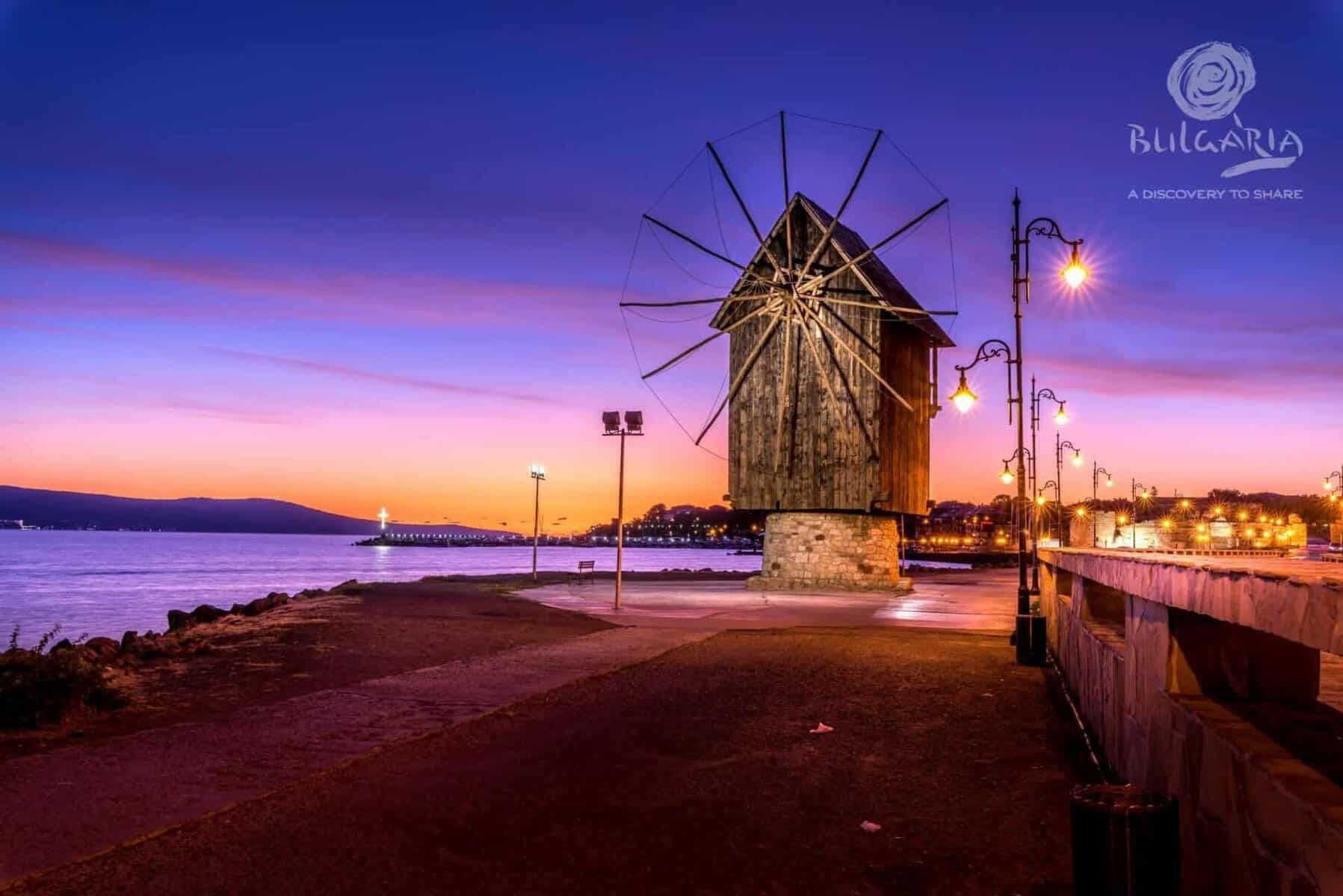 Windmill on beach at sunset, purple sky.