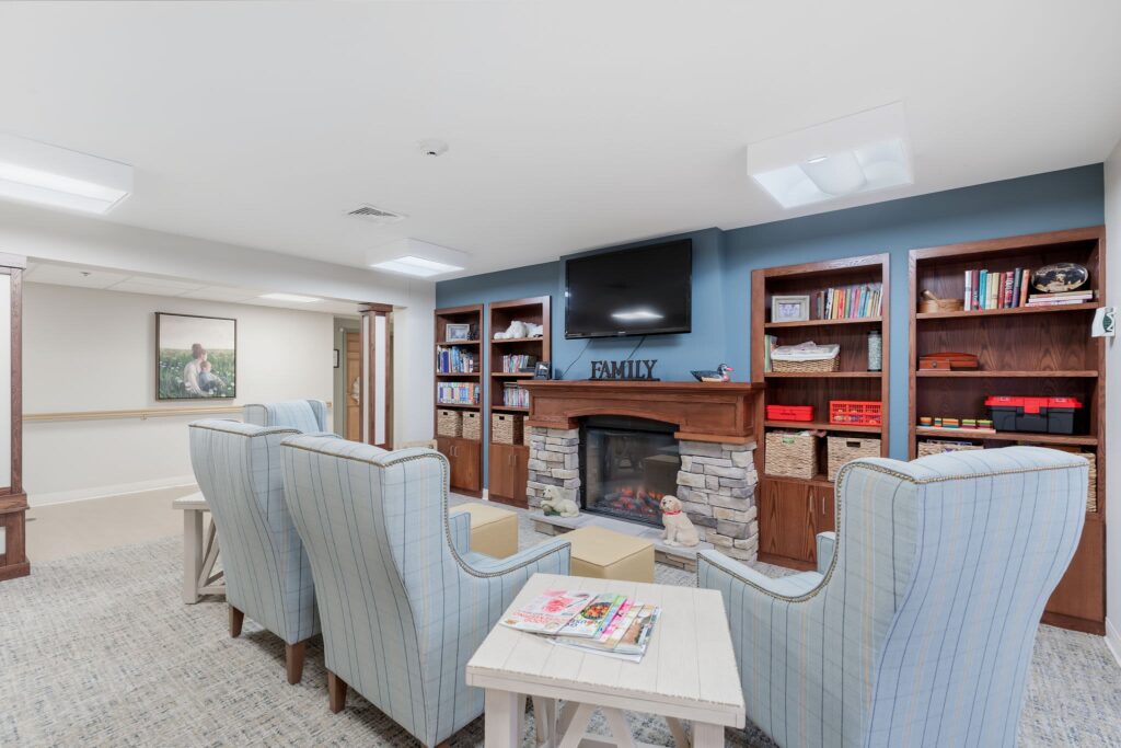 Cozy assisted living community lounge area at Vista Prairie Garnette Gardens in Redwood Falls, featuring a fireplace, comfortable seating, and built-in bookshelves for relaxation and socialization.
