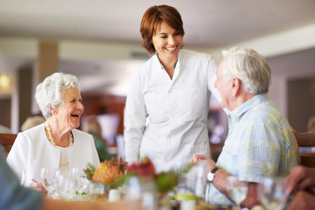 Senior woman and man enjoying a meal with caregiver at Vista Prairie at Garnette Gardens senior living community, emphasizing quality care and vibrant social life for seniors in Redwood Falls, MN.