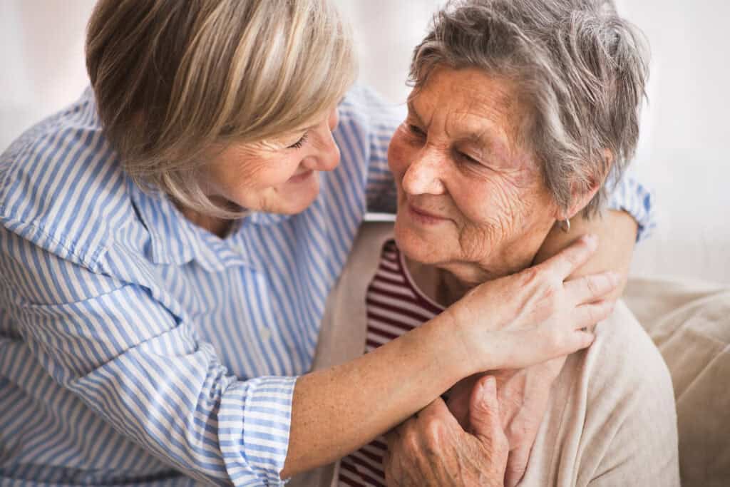 A caring elderly woman embracing a loving visitor, showing warmth and companionship in a cozy home setting.