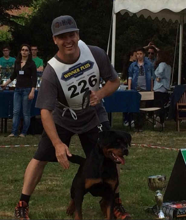 Active man smiling with Rottweiler, participating in a dog agility or competition event.