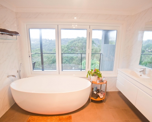 Bright bathroom featuring a white freestanding bathtub and expansive windows with scenic views.