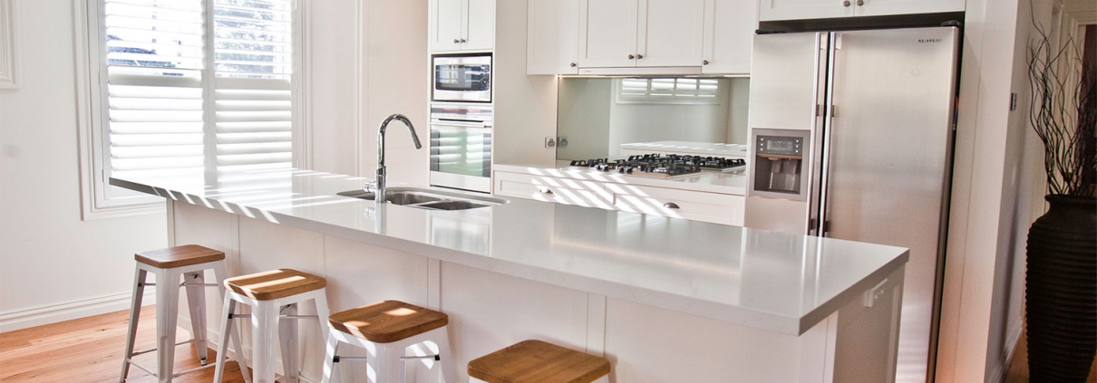 Bright, contemporary kitchen with white cabinetry, island, and wooden bar stools in a Sydney home.