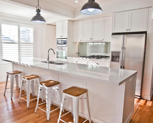 Bright, contemporary kitchen with white cabinetry, island, and wooden bar stools in a Sydney home.