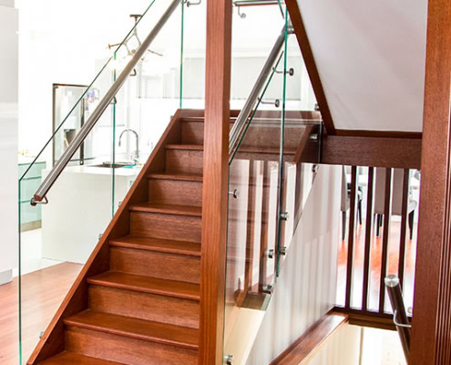 Modern wooden staircase with glass and metal handrails in a residential interior.